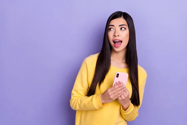 Foto van vrolijk verbaasd gek meisje kijken lege ruimte zie nieuwe telefoon promotie geïsoleerd op violette kleur achtergrond — Stockfoto