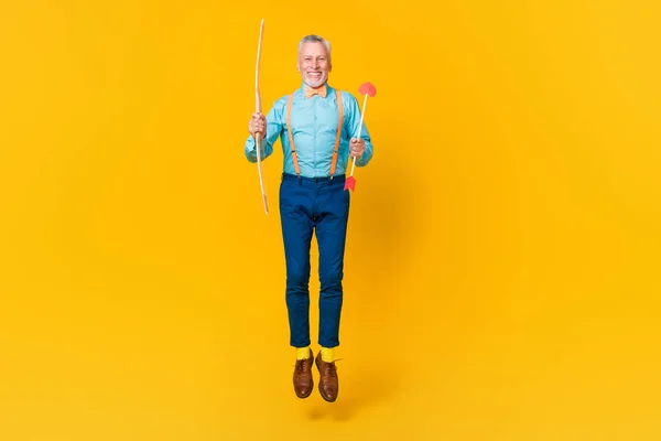 Foto van funky vrolijke man gepensioneerde gekleed teal shirt bowtie springen schieten harten geïsoleerde gele kleur achtergrond — Stockfoto