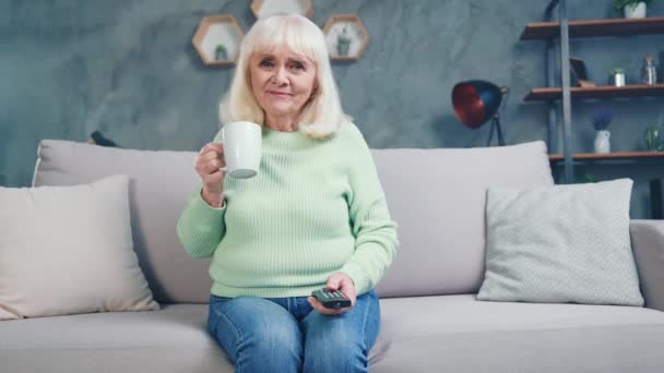 Lustige bequeme Oma halten heißen Becher Getränk schalten Sie den Fernseher überglücklich Haus — Stockvideo
