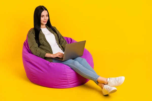 Foto de tamaño completo de la señora joven inteligente sentarse en el tipo de bolso portátil usar camisa jeans zapatos aislados en el fondo amarillo —  Fotos de Stock