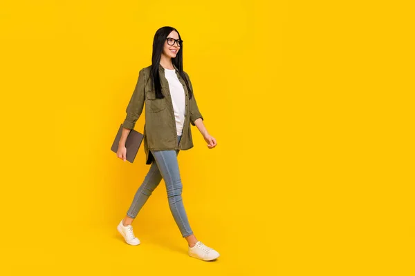 Full size photo of cute young lady hold laptop go wear spectacles shirt jeans footwear isolated on yellow background — Stock Photo, Image