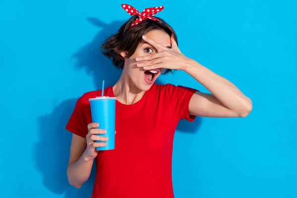 Fénykép vicces fiatal barna hölgy közel arc ital kopás piros póló fejpánt elszigetelt kék színű háttér — Stock Fotó