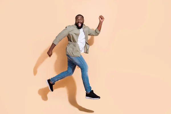 Full kropp profil foto av hurra ung brunett kille kör skrika bära skjorta jeans skor isolerad på beige bakgrund — Stockfoto