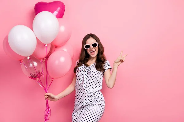 Foto di impressionato donna carina indossare bianco vestito occhiali scuri mostrando v-segno tenendo palloncini isolato colore rosa sfondo — Foto Stock