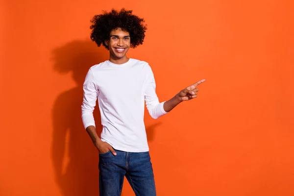 Foto de dulce chico encantador usar camisa blanca señalando dedo vacío espacio aislado color naranja fondo — Foto de Stock
