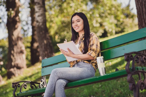 Foto di graziosa giovane donna vestita camicia a quadri seduta panchina scrittura copybook sorridente fuori dalla natura di campagna — Foto Stock