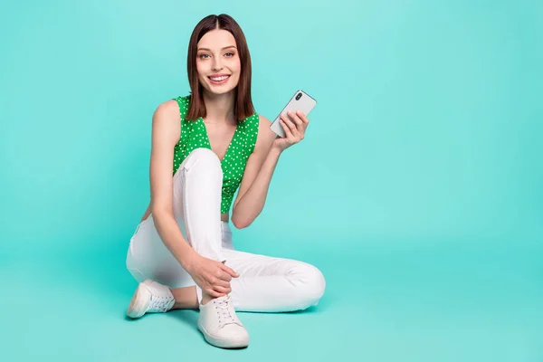 Volledige lengte foto van jonge mooie dame zittende vloer hold mobiele telefoon verslaafde gebruiker geïsoleerd over turquoise kleur achtergrond — Stockfoto