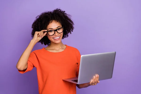 Foto van onder de indruk jonge brunette dame houden laptop dragen oranje t-shirt geïsoleerd op paarse achtergrond — Stockfoto
