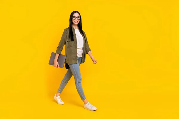 Foto de longitud completa de la señora del milenio agradable celebrar portátil ir usar gafas camisa jeans zapatillas aisladas sobre fondo amarillo —  Fotos de Stock