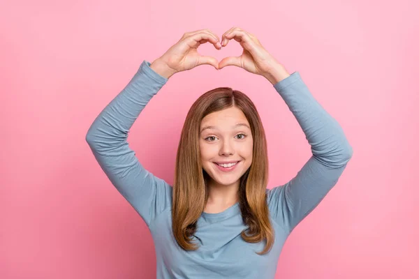 Retrato de atraente carinhoso alegre menina de cabelos castanhos mostrando sinal do coração isolado sobre cor pastel rosa fundo — Fotografia de Stock