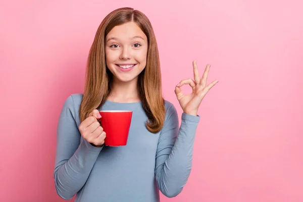 Портрет привлекательной веселой веселой девушки, пьющей какао, показывающий хорошо знаком изолированы на розовом пастельном фоне — стоковое фото