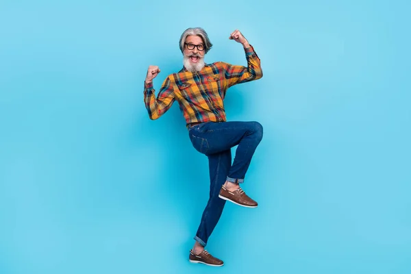 Foto de homem atraente sorte desgaste xadrez camisa óculos andando levantando punhos isolado azul cor fundo — Fotografia de Stock