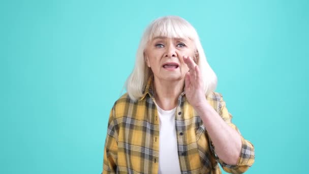 パニック老婦人波手ジェスチャーは、孤立したシアン色の背景を助けを求める — ストック動画