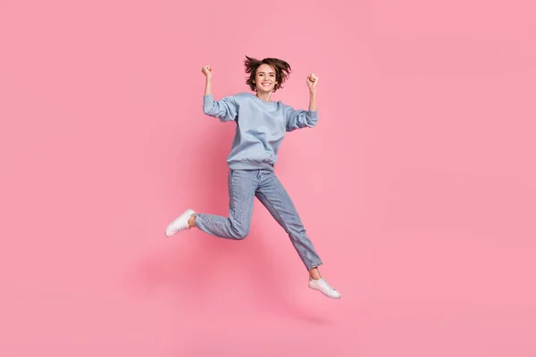 젊은 여성 이 점프를 축하하는 사진 전체가 핑크 색 배경에 고립된 점퍼 청바지 신발을 착용하고 있다 — 스톡 사진