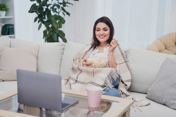 Retrato de una atractiva mujer alegre enfocada sentada en diván comiendo palomitas de maíz viendo películas de televisión en casa en interiores — Foto de Stock