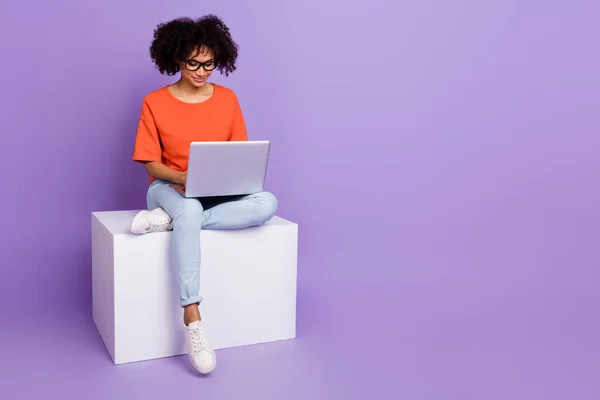 Piena lunghezza foto di intelligente signora millenaria sedersi sul cubo tipo laptop usura t-shirt jeans scarpe isolate su sfondo viola — Foto Stock