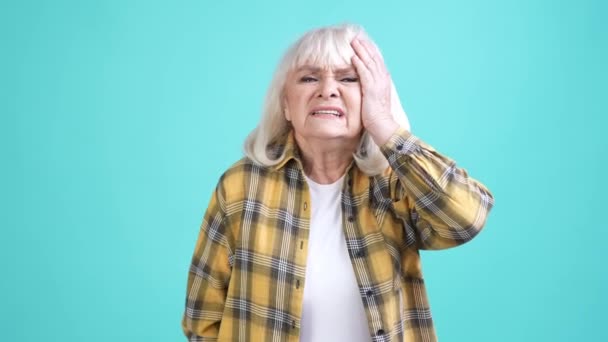 La abuela se siente poco saludable sufren dolor de cabeza severo aislado fondo de color cian — Vídeo de stock