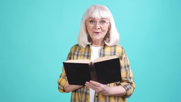 Inteligente abuelita tiempo libre leer interesante libro aislado cyan color fondo — Vídeo de stock