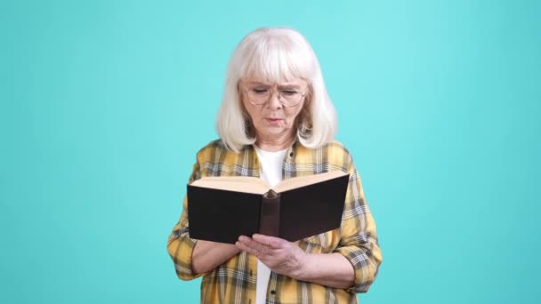 Nenek berkonsentrasi membaca buku teks terisolasi cyan warna latar belakang — Stok Video
