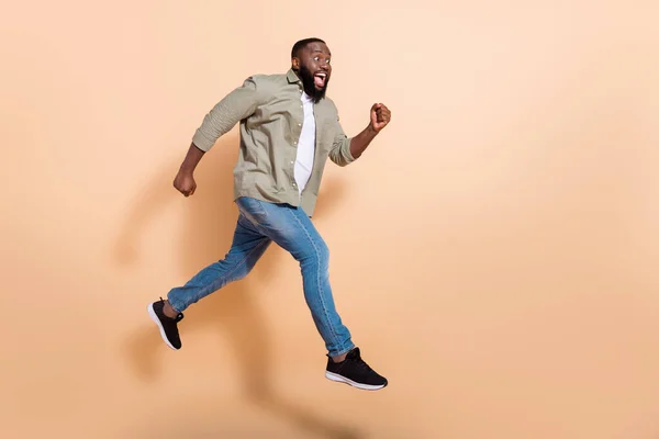 Full size profil fotografie ohromen tisíciletý brunet chlap skok křičet nosit košili džíny tenisky izolované na béžové pozadí — Stock fotografie