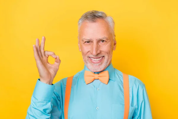 Foto de viejo gris peinado hombre mostrar okey desgaste camiseta verde tirantes pajarita aislado sobre fondo de color amarillo —  Fotos de Stock