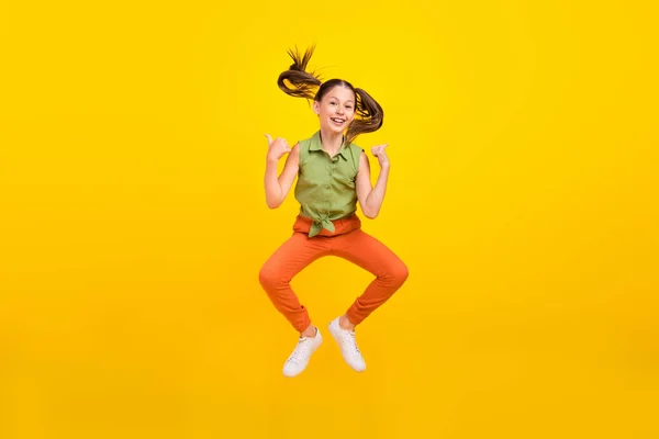 예쁜 여학생이 웃으며 녹색 셔츠를 입고 있고 외진 노란색 배경을 점프하는 눈물을 보여 주고 있는 사진 — 스톡 사진