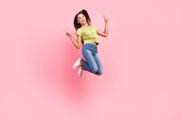 Foto de amigable señora salto espectáculo v-signos divertirse desgaste verde superior jeans calzado aislado de color rosa fondo —  Fotos de Stock