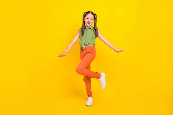 Foto de niña preadolescente infantil divertida vestida verde superior caminando sonriente aislado color amarillo fondo —  Fotos de Stock