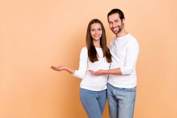 Photo of nice millennial brunette couple hold empty space wear white cloth isolated on beige color background — Stock Photo, Image