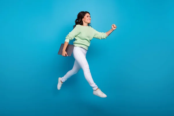 Tamanho do corpo de comprimento total vista de mulher alegre atraente pulando segurando laptop indo isolado sobre fundo de cor azul brilhante — Fotografia de Stock