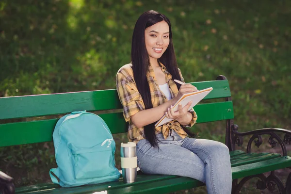 Foto di carino affascinante giovane donna vestita camicia a quadri seduta panchina scrittura copybook sorridente fuori natura paesaggio — Foto Stock