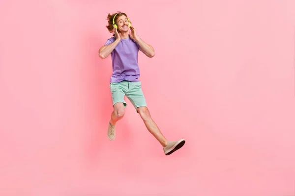 Volledige lichaamsomvang uitzicht van aantrekkelijke vrolijke man springen luisteren hit lied geïsoleerd over roze pastel kleur achtergrond — Stockfoto