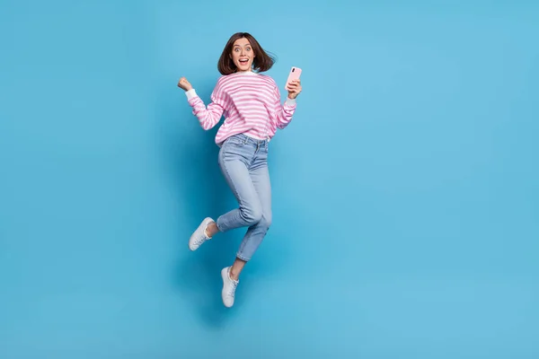 Full body photo of impressed millennial lady jump with phone call wear shirt jeans sneakers απομονωμένα σε μπλε φόντο — Φωτογραφία Αρχείου