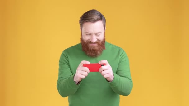 Ενθουσιασμένη κοκκινομάλλα τύπος παίζουν συσκευή γροθιά επάνω απομονωμένο ζωντανό φόντο χρώμα — Αρχείο Βίντεο