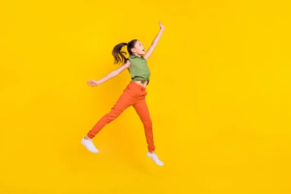 Foto de excitada linda niña preadolescente vestida verde superior saltando brazo de alta captura espacio vacío sonriendo aislado color amarillo fondo —  Fotos de Stock