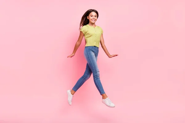 Foto de alegre linda chica salto ir posando ropa verde top jeans zapatillas aisladas de color rosa fondo —  Fotos de Stock