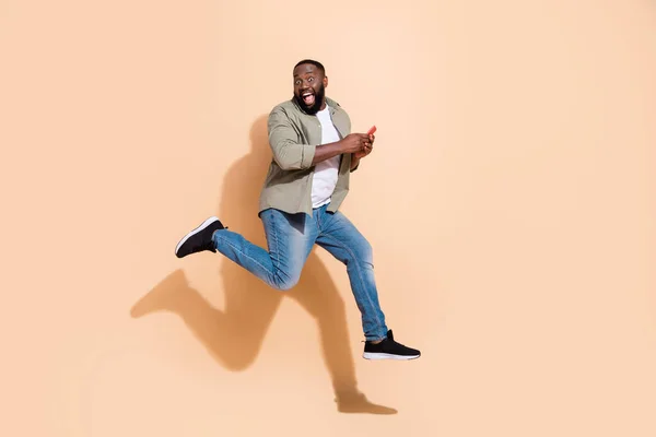 Фотография в полный рост впечатлительного брюнета, бегущего по телефону в джинсовых туфлях на бежевом фоне — стоковое фото