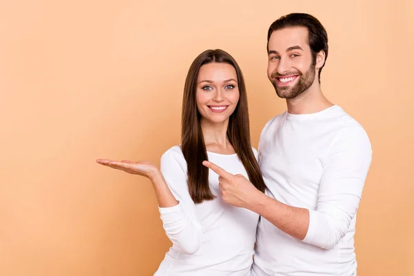 Photo of cute young brunette couple hold index empty space wear white cloth isolated on beige color background — Stock Photo, Image