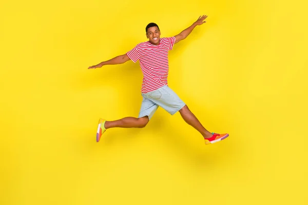 Pleine longueur profil côté photo de gars saut lever les mains côté course usure rouge rayé chaussures isolées sur fond de couleur jaune — Photo