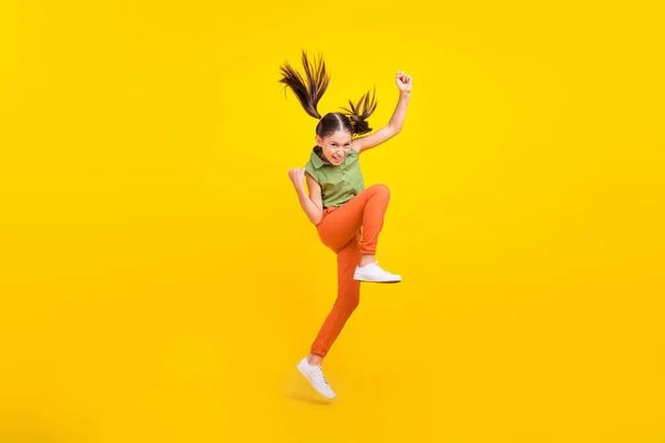 Zdjęcie słodkie szczęście nastolatka dziewczyna ubrana zielony góry skoki wysoki wschodzące pięści uśmiechając się odizolowany żółty kolor tło — Zdjęcie stockowe
