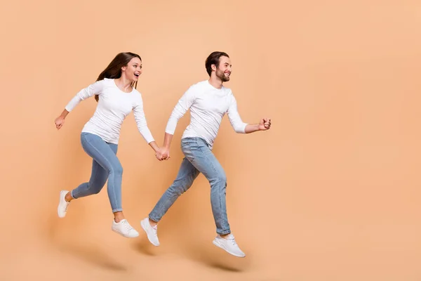 Tamanho total do corpo vista de parceiros alegres atraentes pulando de mãos dadas indo isolado sobre fundo cor pastel bege — Fotografia de Stock