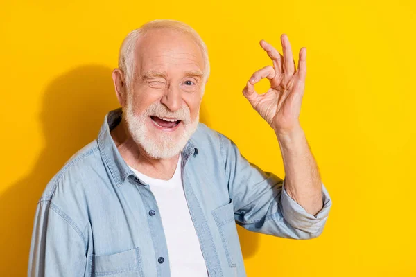 Portret van aantrekkelijke vrolijke grijsharige man tonen ok-teken eens ad knipperen geïsoleerd over helder gele kleur achtergrond — Stockfoto