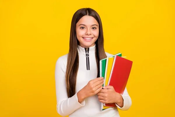 Foto de adorável doce estudante menina desgaste branco zip shirt sorrindo segurando copybooks isolado cor amarela fundo — Fotografia de Stock