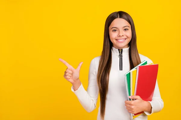 Foto de estudante adorável brilhante vestir camisa branca zip sorrindo segurando diários apontando espaço vazio isolado cor amarela fundo — Fotografia de Stock
