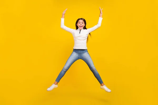 Volledige foto van coole brunette klein meisje springen slijtage trui jeans sneakers geïsoleerd op geel kleur achtergrond — Stockfoto
