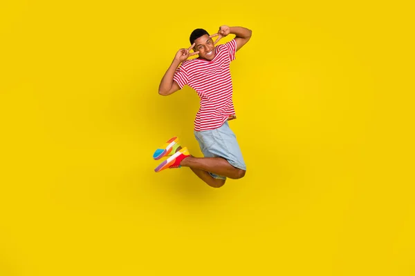 Full body photo of guy jump make v-sign eye wear red striped t-shirt short isolated over bright yellow color background — Fotografia de Stock