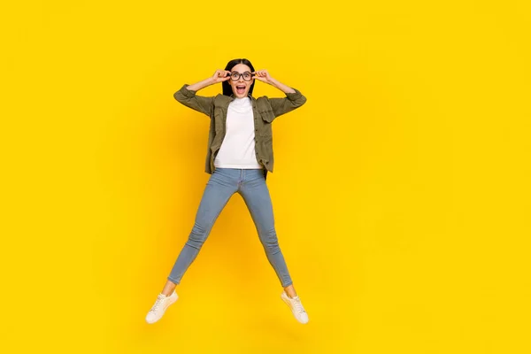 Full längd foto av imponerad ung dam hoppa slitage glasögon skjorta jeans skor isolerad på gul bakgrund — Stockfoto