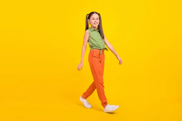 Foto av ganska bedårande preteen flicka klädd grön topp promenader ler isolerad gul färg bakgrund — Stockfoto