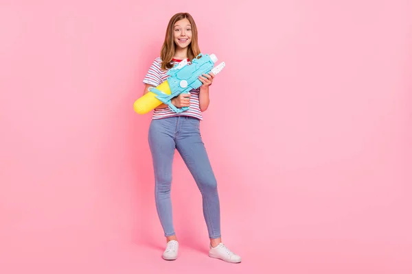 Foto in voller Größe von netten jugendlichen blonden Mädchen schießen aus Gewehr tragen T-Shirt Jeans Schuhe isoliert auf rosa Hintergrund — Stockfoto