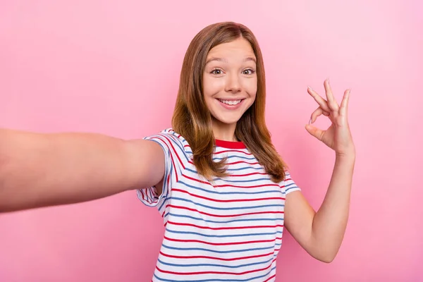 Foto de linda niña pequeña hacer selfie show okey desgaste camiseta roja aislada sobre fondo de color rosa — Foto de Stock